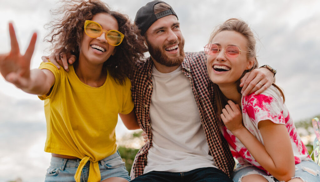 happy young company of smiling friends sitting in park